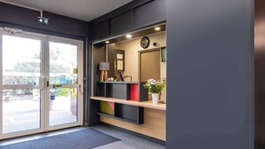 A modern reception area with a glass door entrance, a clock, and a shelf with a potted plant. - B&B HOTEL Valence Sud (Valence)