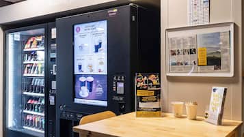 A self-service beverage machine with a digital menu, a seating area with a table, and informational posters on the wall.