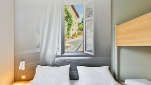 A bedroom with a bed, a nightstand, a window with a view of a street, and a wooden headboard. - B&B HOTEL Valence Sud (Valence)