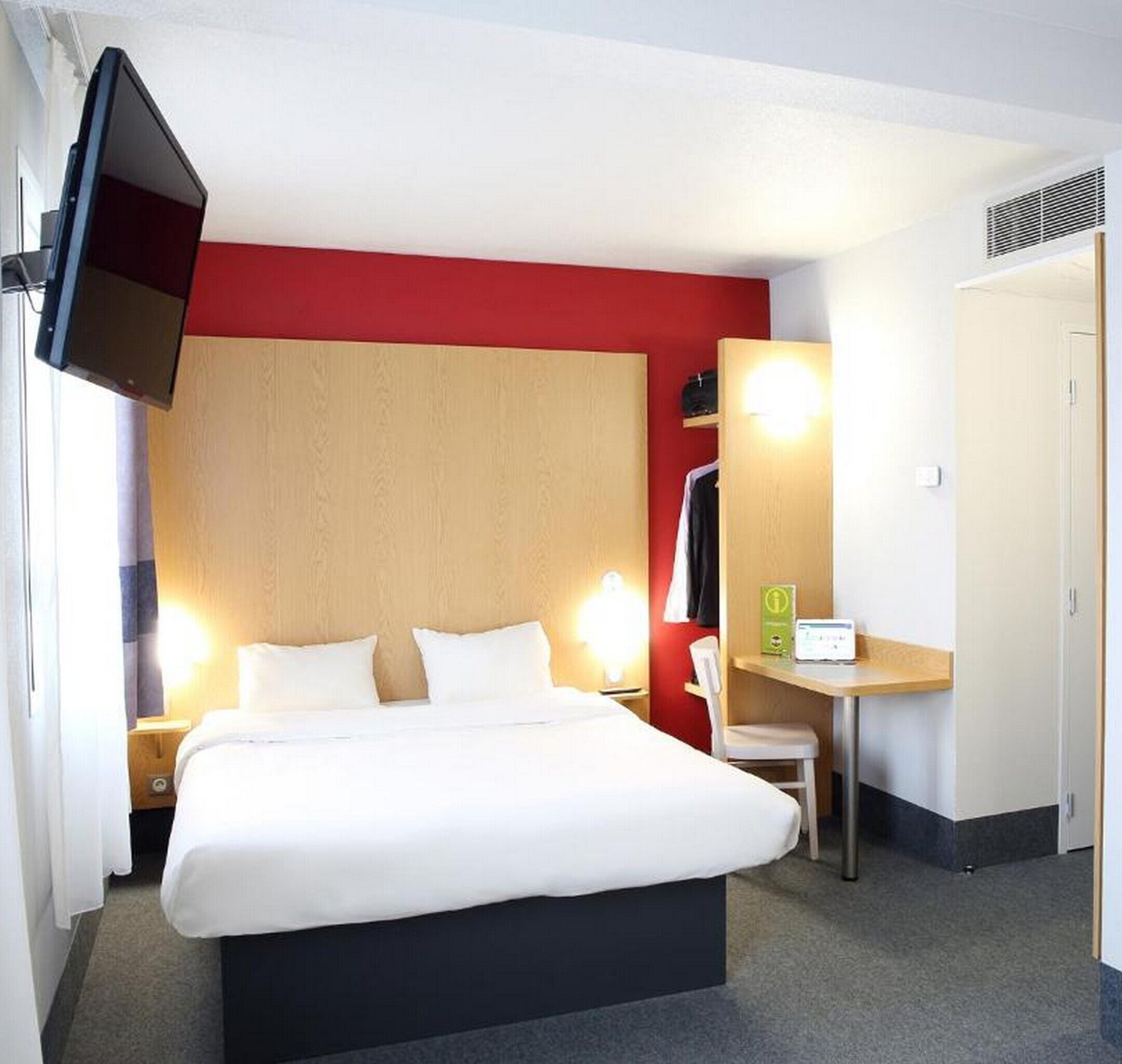 Une chambre d’hôtel comprenant un lit, des lampes de chevet, un bureau avec un ordinateur, une télévision et une armoire.