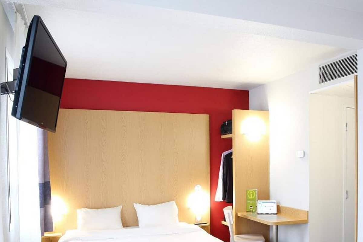 Una habitación de hotel con cama, lámparas de noche, un escritorio con computadora, televisión y armario.