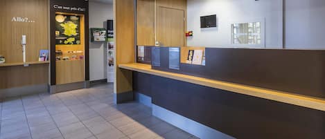 Un área de recepción con un mostrador de madera, un cartel que dice 'Bienvenue chez', un teléfono y carteles informativos.