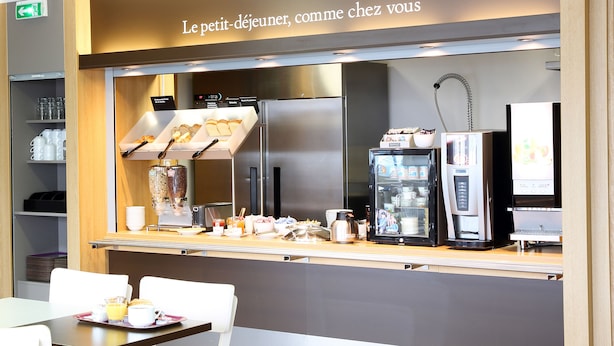 A breakfast bar with a coffee machine, refrigerator, and shelves with cups and bowls. - B&B HOTEL Perpignan Sud Marché International (Perpignan)