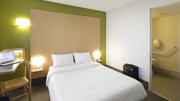Habitació d'hotel amb llit, escriptori amb un portàtil, cadira, maleta i bany amb vàter i dutxa.