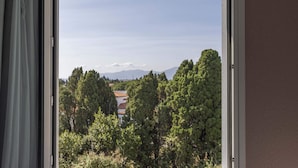 A view through an open window with a mountain in the background and trees in the foreground. - B&B HOTEL Perpignan Sud Marché International (Perpignan)