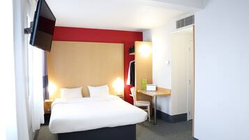 A hotel room with a bed, a desk, a chair, a TV, and a door.