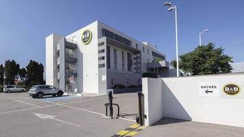 A modern B&B hotel with a white facade, a blue parking bay, and a clear sky.