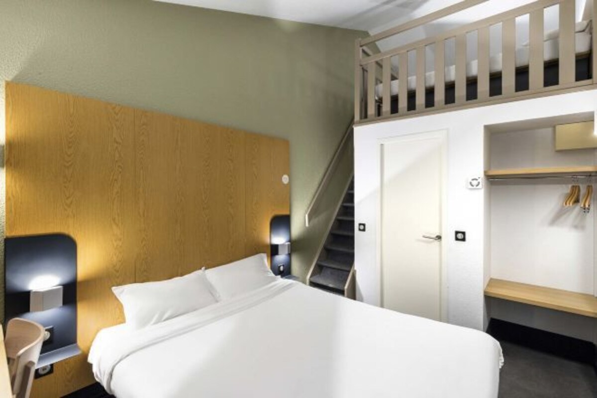 Une chambre d’hôtel comprenant un lit, une tête de lit en bois, une table de chevet avec une lampe, un escalier et une armoire.