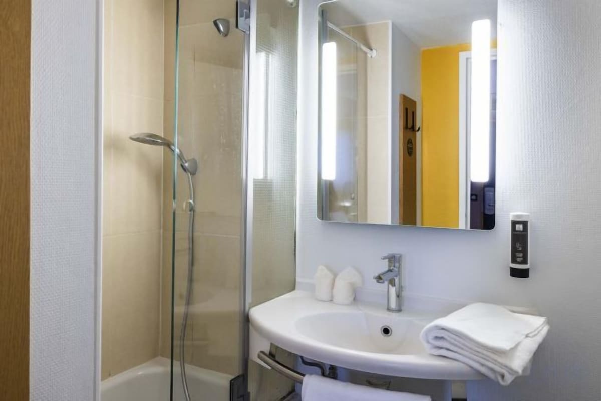 Un baño con ducha de vidrio, un lavabo blanco y un espejo con luz superior.
