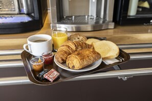Ein Tablett mit Croissants, einem Glas Orangensaft, einer Tasse Kaffee und einer kleinen Marmeladendose.