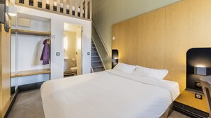 Una habitación de hotel con una cama grande, cabecera de madera, armario empotrado y una escalera que lleva a un nivel superior.