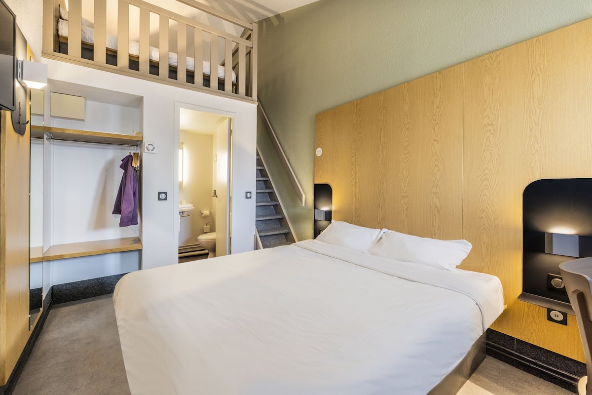 Una habitación de hotel con una cama grande, cabecera de madera, armario empotrado y una escalera que lleva a un nivel superior.