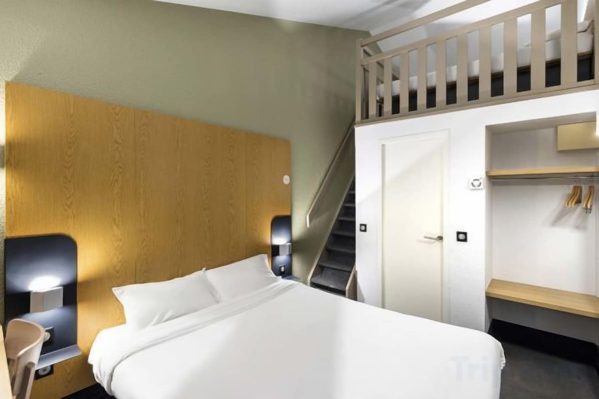 Una habitación de hotel con cama, mesita de noche, escritorio, armario y una escalera.