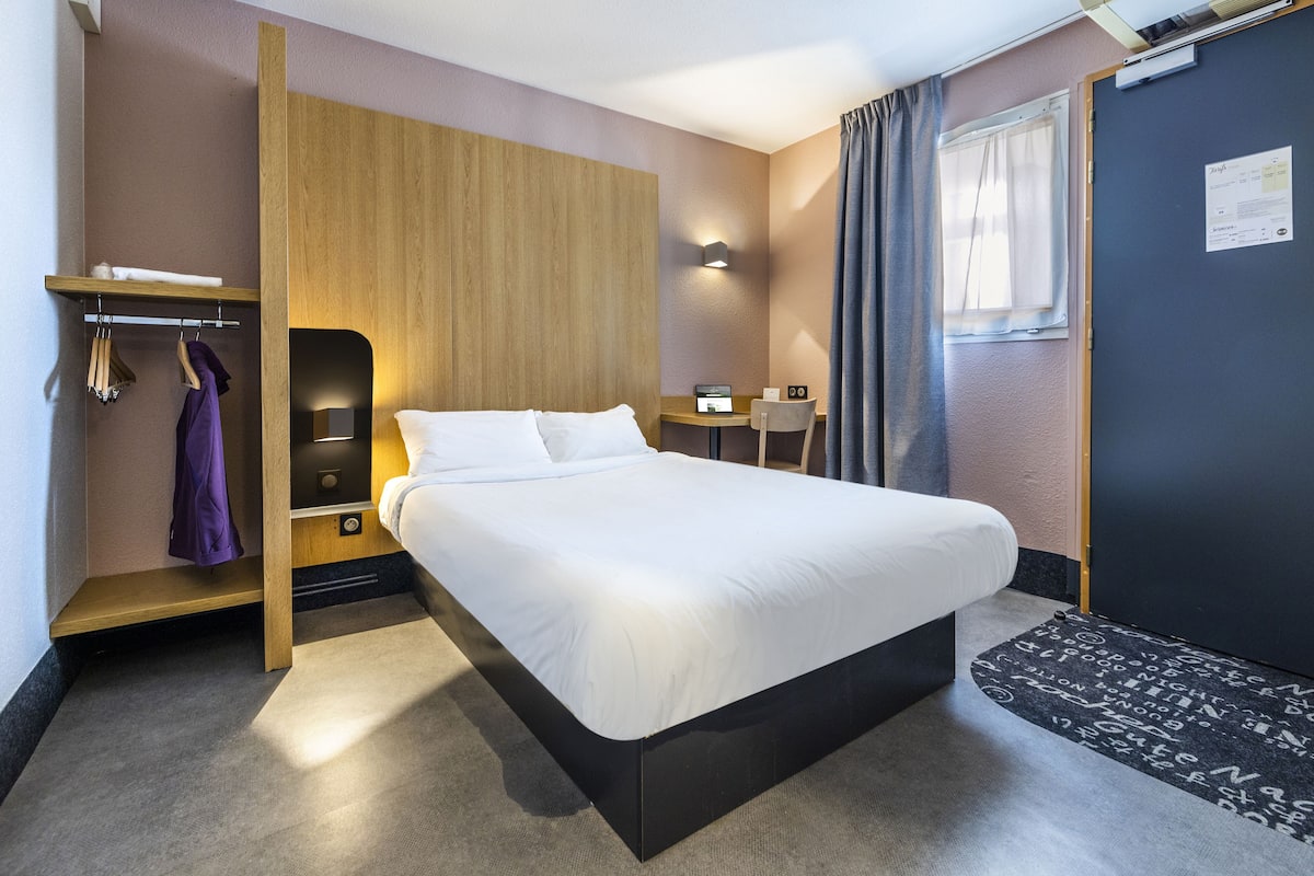 Una habitación de hotel moderna con una cama grande, un escritorio, una silla y un armario.