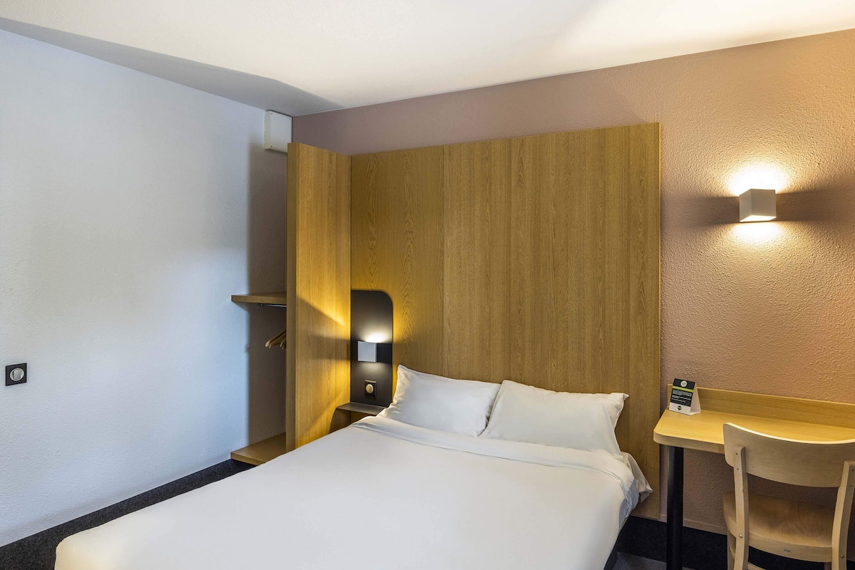 Habitación de hotel con cama, escritorio y una silla. Un aplique está fijado a la pared sobre el escritorio.