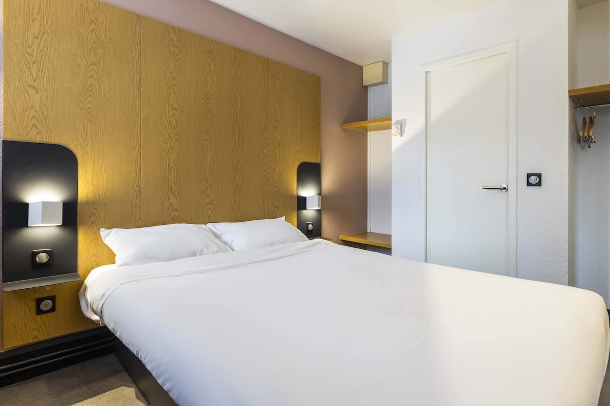 Habitación de hotel con una cama grande, cabecero de madera, lámparas de noche y una puerta con picaporte.