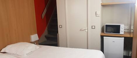 Un dormitorio con cama, microondas y refrigerador.