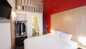 A hotel room with a bed, a TV, a closet, a bathroom, and a staircase.