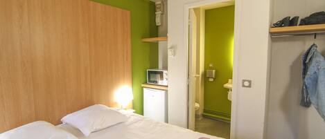 A hotel room with a bed, a microwave, a small refrigerator, and a door leading to a bathroom.