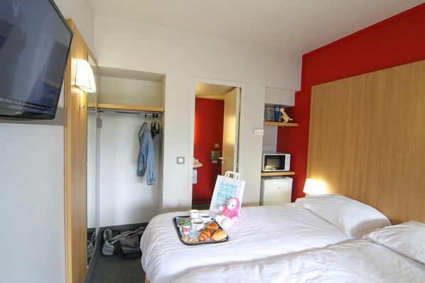 A hotel room with a bed, a TV, a tray with breakfast items, and a red wall.
