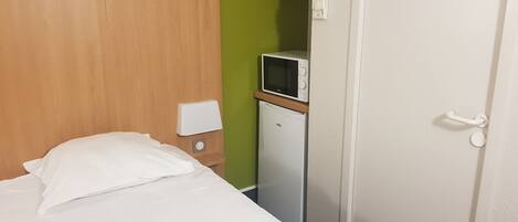 A hotel room with a bed, a small refrigerator, a microwave, and a white door.