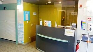 A reception desk with a glass partition, a closed door, and various informational posters.