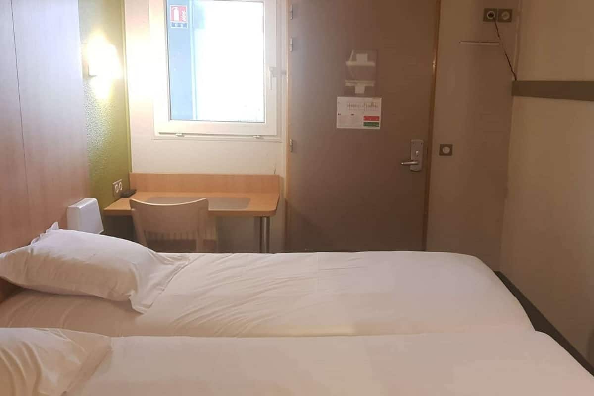 Una habitación de hotel con cama, un escritorio pequeño con silla, ventana y puerta.
