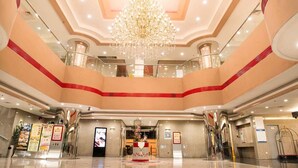 Een hotellobby met meerdere verdiepingen, een grote kroonluchter en een centrale receptie.