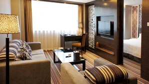 Een hotelkamer met een zithoek, een bureau met stoel, een aan de muur bevestigde televisie en een bed.
