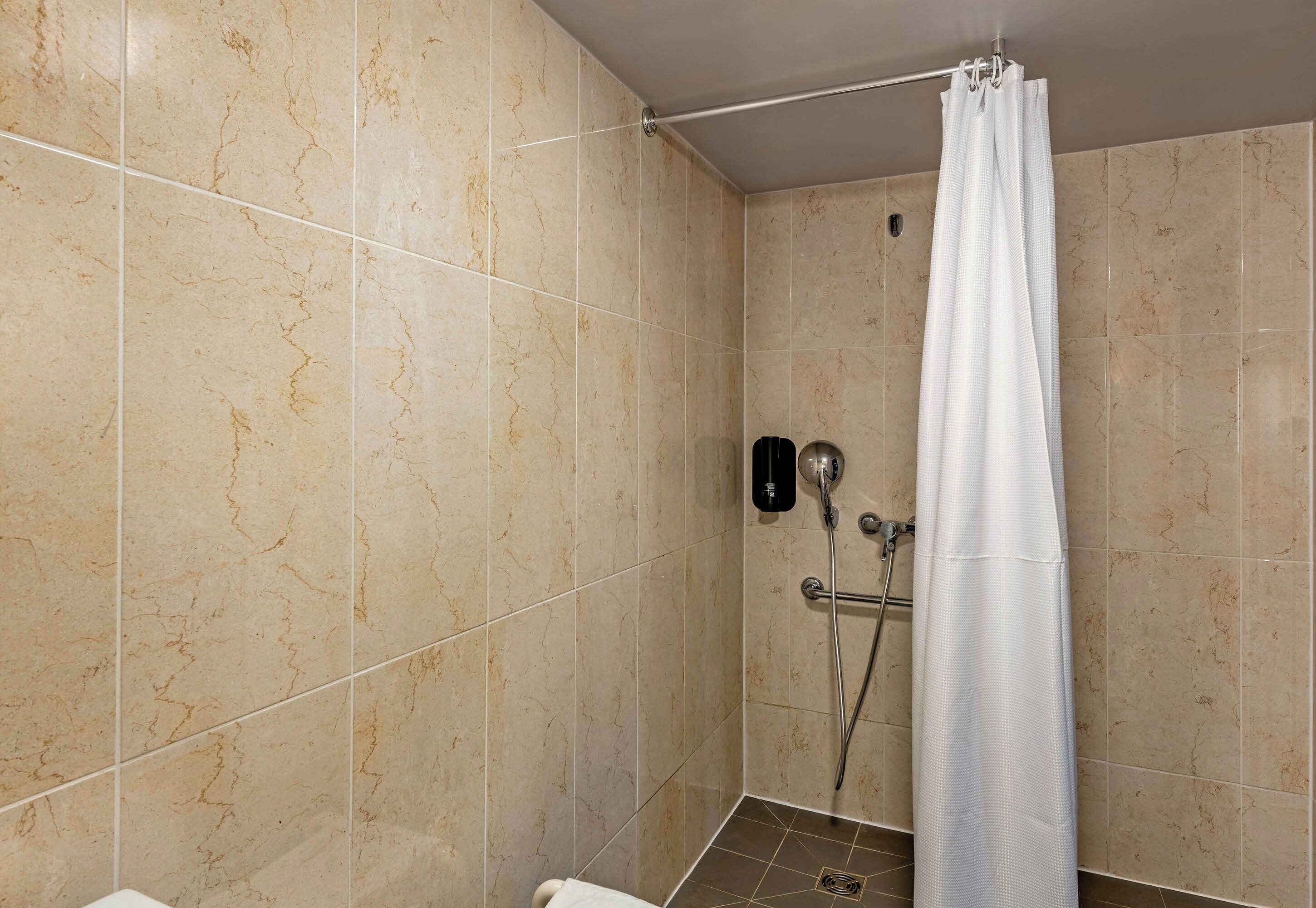 Ducha con cortina blanca, cabezal de ducha de mano y grifo empotrado en la pared.