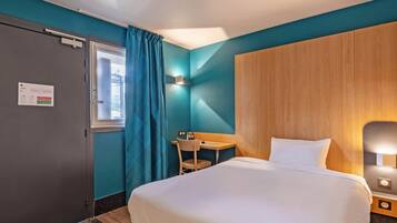 Ein Hotelzimmer mit einem Bett, einem Schreibtisch, einem Stuhl und einem fensterbepflanzten Fenster.