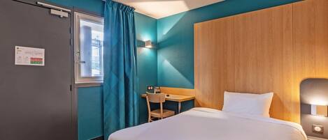 A hotel room with a bed, a desk, a chair, and a window with curtains.