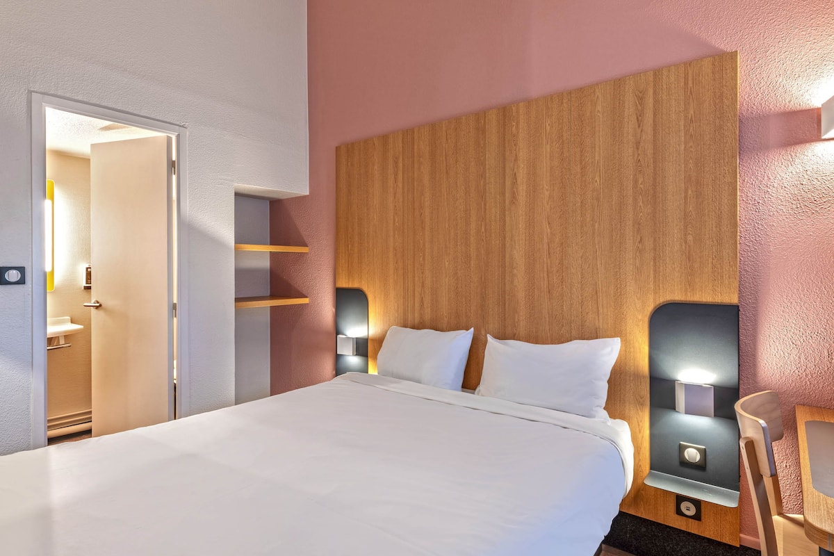 Hotelkamer met een groot bed, houten hoofdeinde, bedlampjes en een deur naar een badkamer.