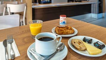 A breakfast setting with a cup of coffee, a glass of orange juice, a croissant, a slice of bread, cheese, and jam on a wooden table.