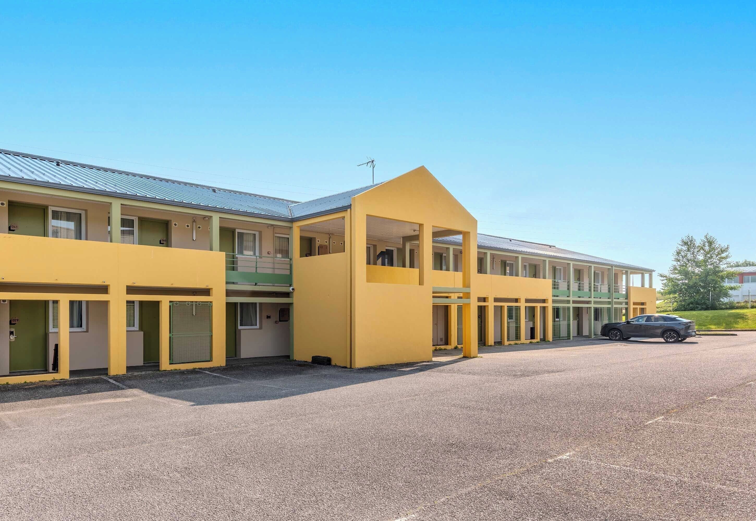 Un motel jaune avec de nombreuses chambres et un espace de stationnement couvert.