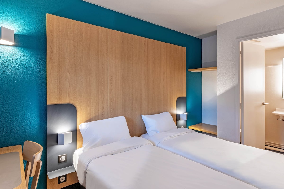 Een hotelkamer met twee bedden, een houten hoofdeinde en wandlampen.