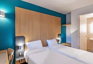 A hotel room with a wooden headboard, two beds, bedside lamps, a nightstand, and a bathroom visible through an open door.