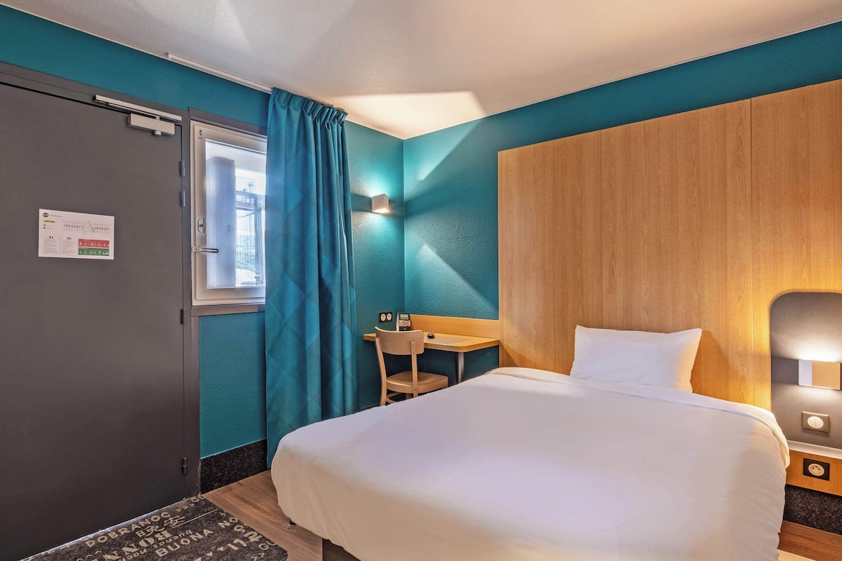 Een hotelkamer met een bed, een bureau, een stoel en een raam met gordijnen.