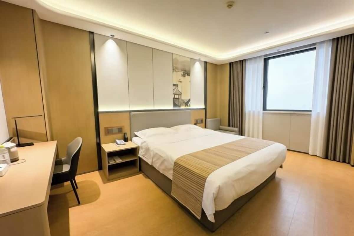 Habitación de hotel con cama, escritorio, silla y un ventanal con cortinas.