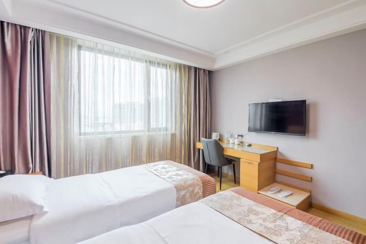 A hotel room with two beds, a desk, a chair, a television, and a window with curtains.