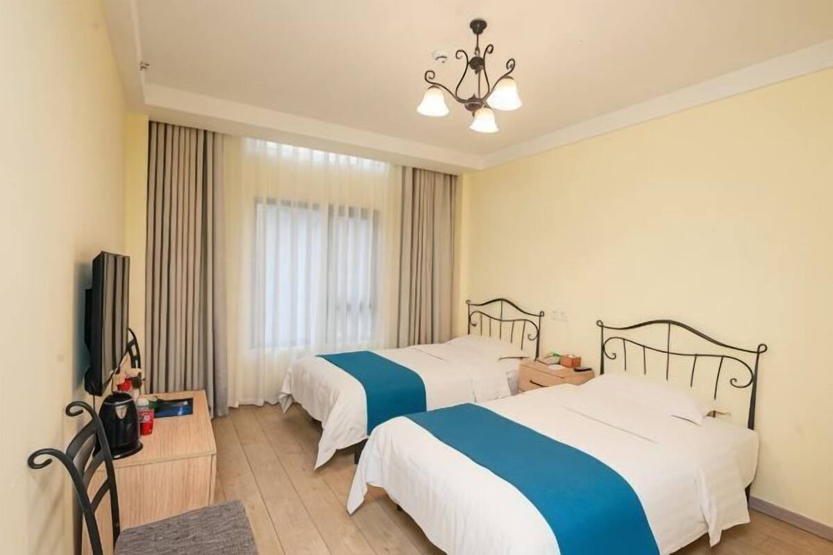 A hotel room with two beds, a desk with a chair, a television, and a chandelier.