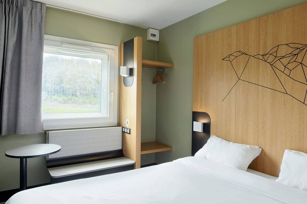 Ein Hotelzimmer mit einem Bett, einem kleinen Tisch, einem Kleiderständer und einem Fenster mit Vorhängen.