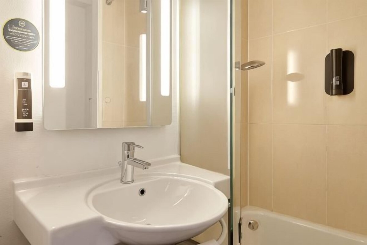 Une salle de bain avec un lavabo blanc, un miroir et une cabine de douche en verre.