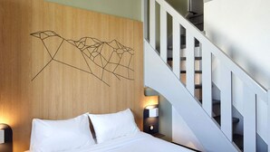 Een hotelkamer met een houten hoofdeinde, een bed met wit beddengoed, twee bedlampen en een trap.