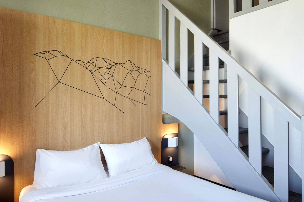 Ein Hotelzimmer mit einem hölzernen Kopfteil, einem Bett mit weißer Bettwäsche, zwei Nachttischlampen und einer Treppe.