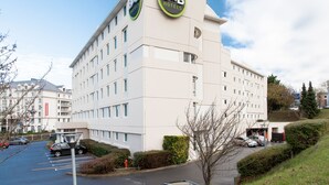 Een B&B hotel met een modern design, herkenbaar aan een logo op de gevel, een parkeerplaats en een verzorgd gazon.