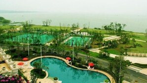 A large swimming pool with a curved design, surrounded by a landscaped area with pathways and greenery. - Country Garden Phoenix Hotel Chaohu (Hefei)