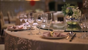 A round dining table with four wine glasses, a vase with flowers, and a plate with a napkin and cutlery. - Country Garden Phoenix Hotel Chaohu (Hefei)