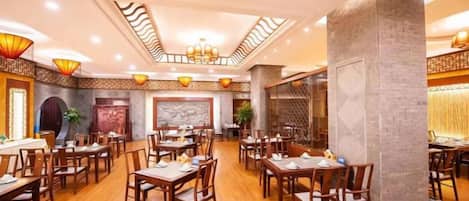 A spacious restaurant with multiple tables and chairs, high ceilings with decorative lighting, and a modern interior design.