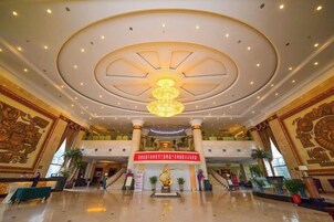 A spacious lobby with a grand chandelier, a central staircase, and ornate wall decorations.